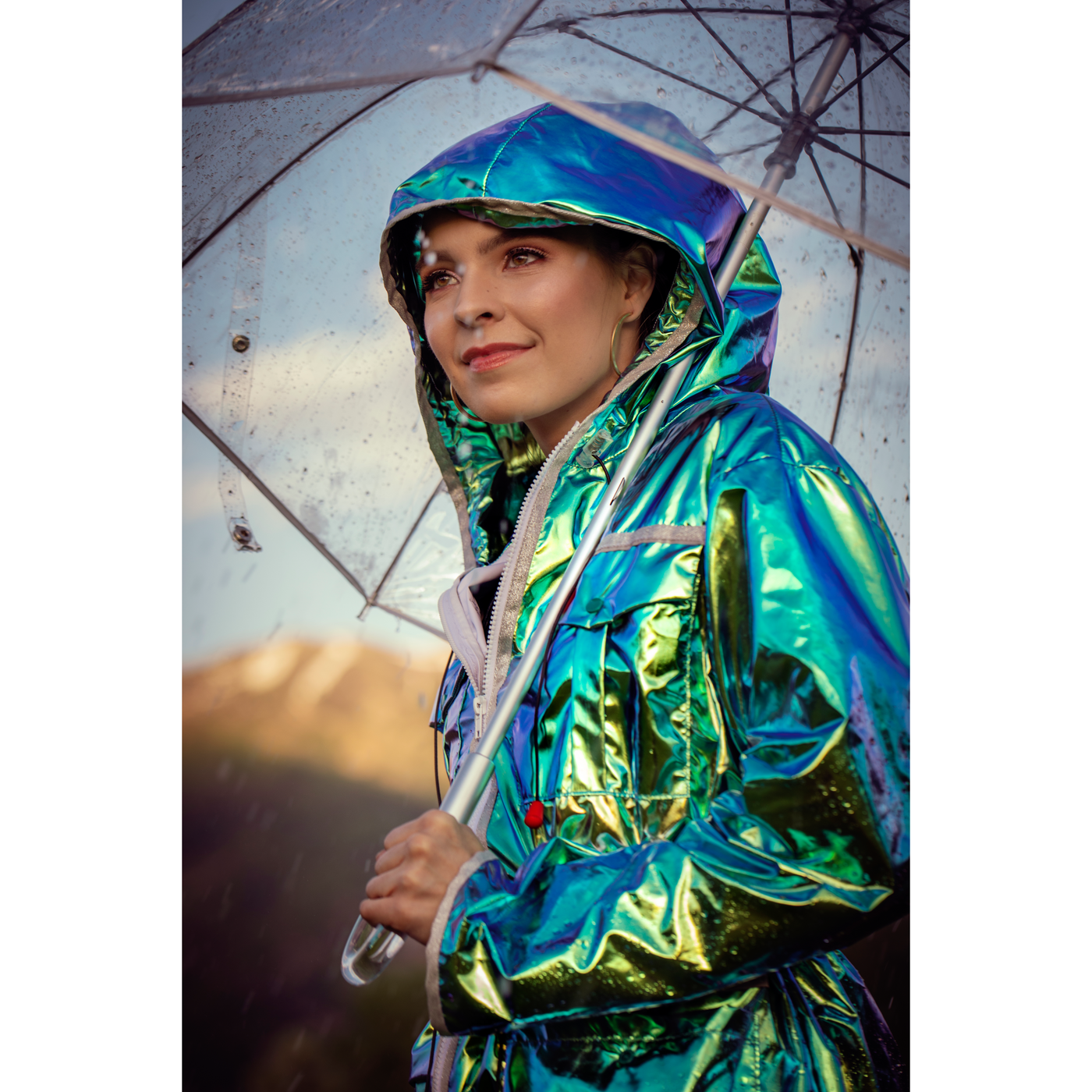 Image of a woman wearing a metallic green women’s mid-season jacket with the hood up in the rain
